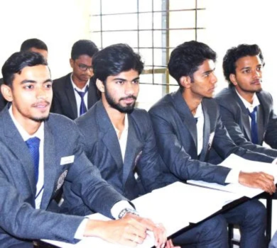 Male students in grey blazers and blue ties sitting at desks and listening in a classroom.