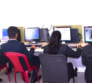 Students working at their computers in the computer lab, sitting in red chairs.