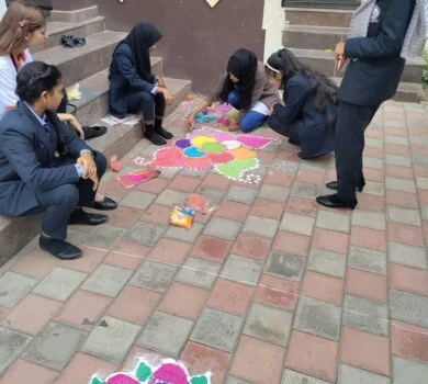 Students sitting on the floor creating a colorful rangoli design.
