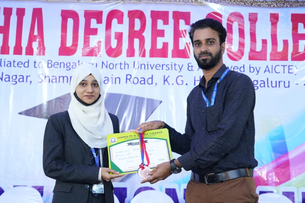 A female graduating student in a white hijab receiving her certificate on stage.