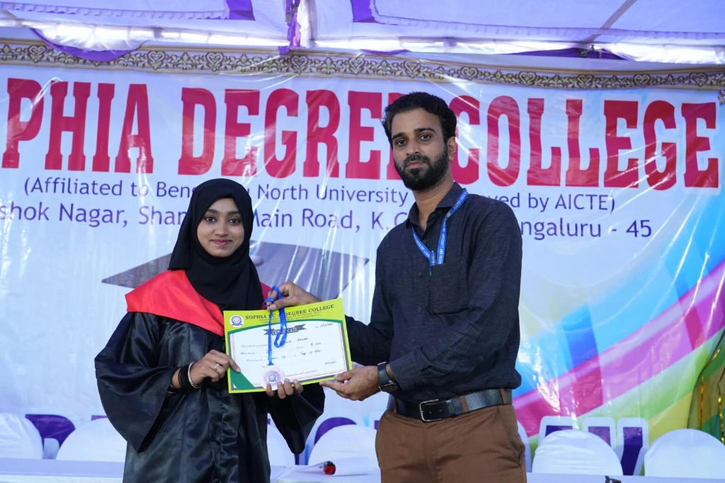 A female graduate in a dark hijab receiving a certificate and medal.