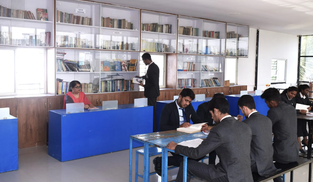Interior of the college library showing bookshelves, students studying at blue desks, and a librarian at the counter.